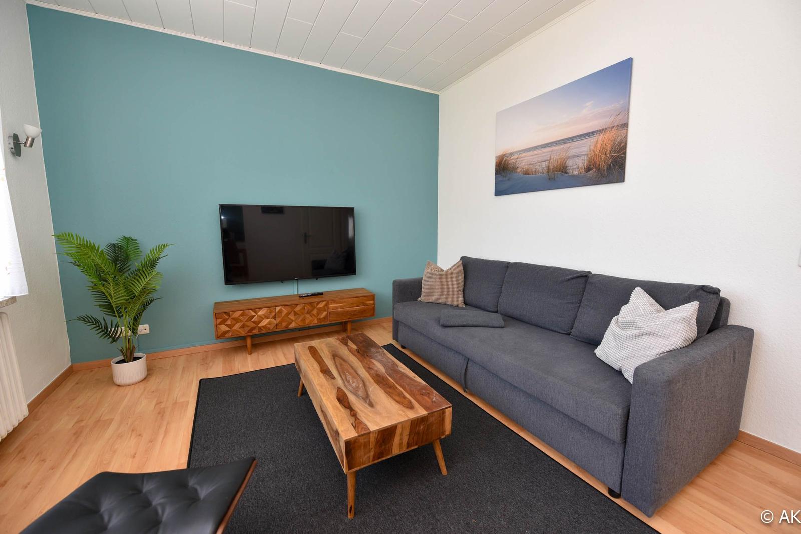 Wohnzimmer mit Sofa, Fernseher und Holztisch.