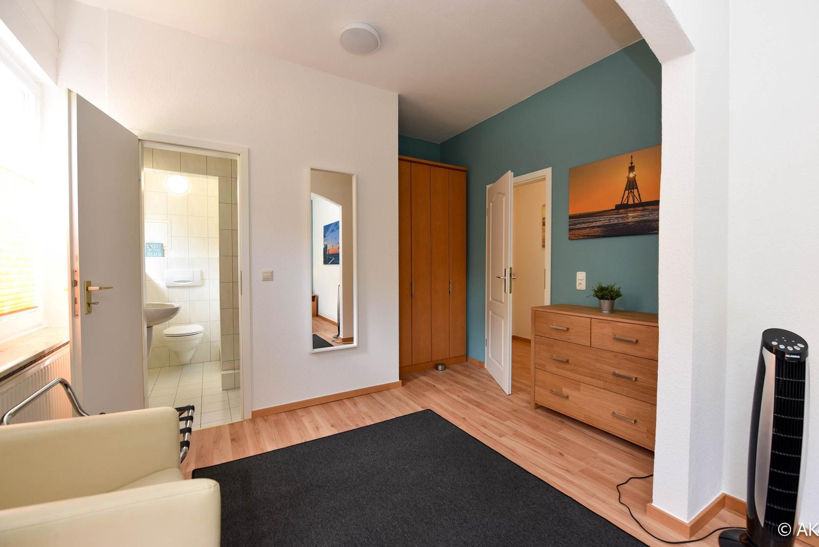 Zimmer mit Holzboden, Schrank, Schminktisch und Bad im Hintergrund.