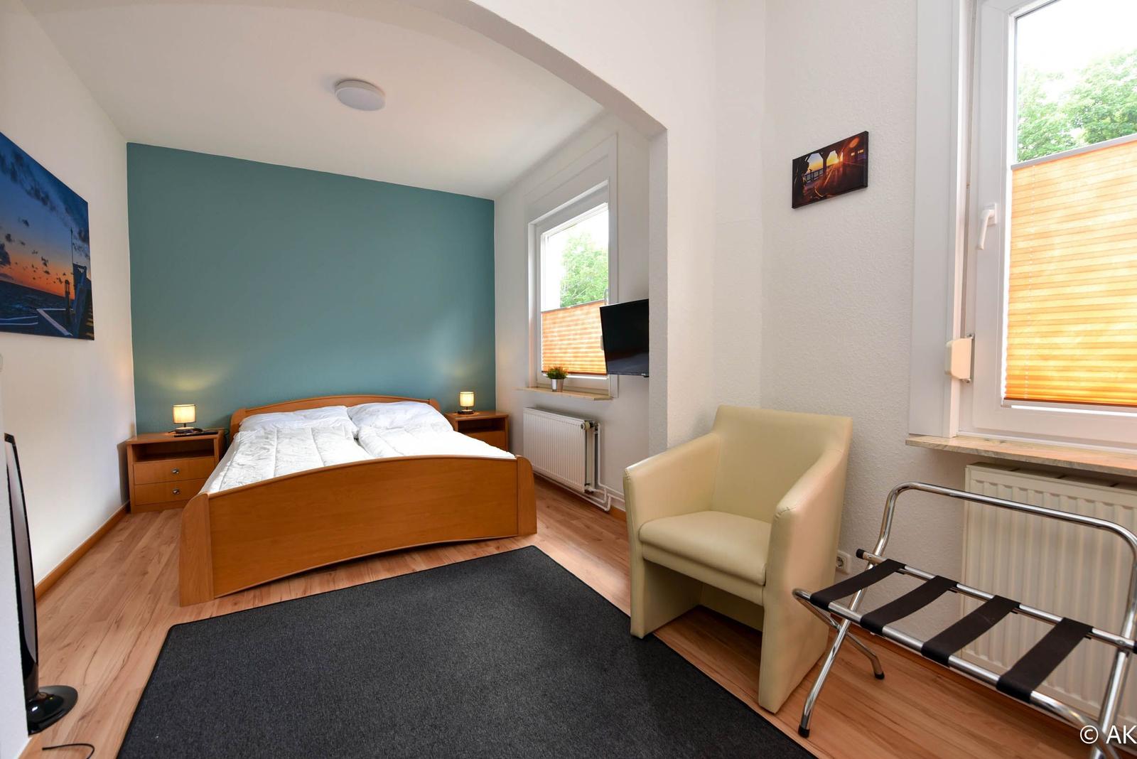 Schlafzimmer mit Bett, Sessel und Fenster mit Blick nach draußen.