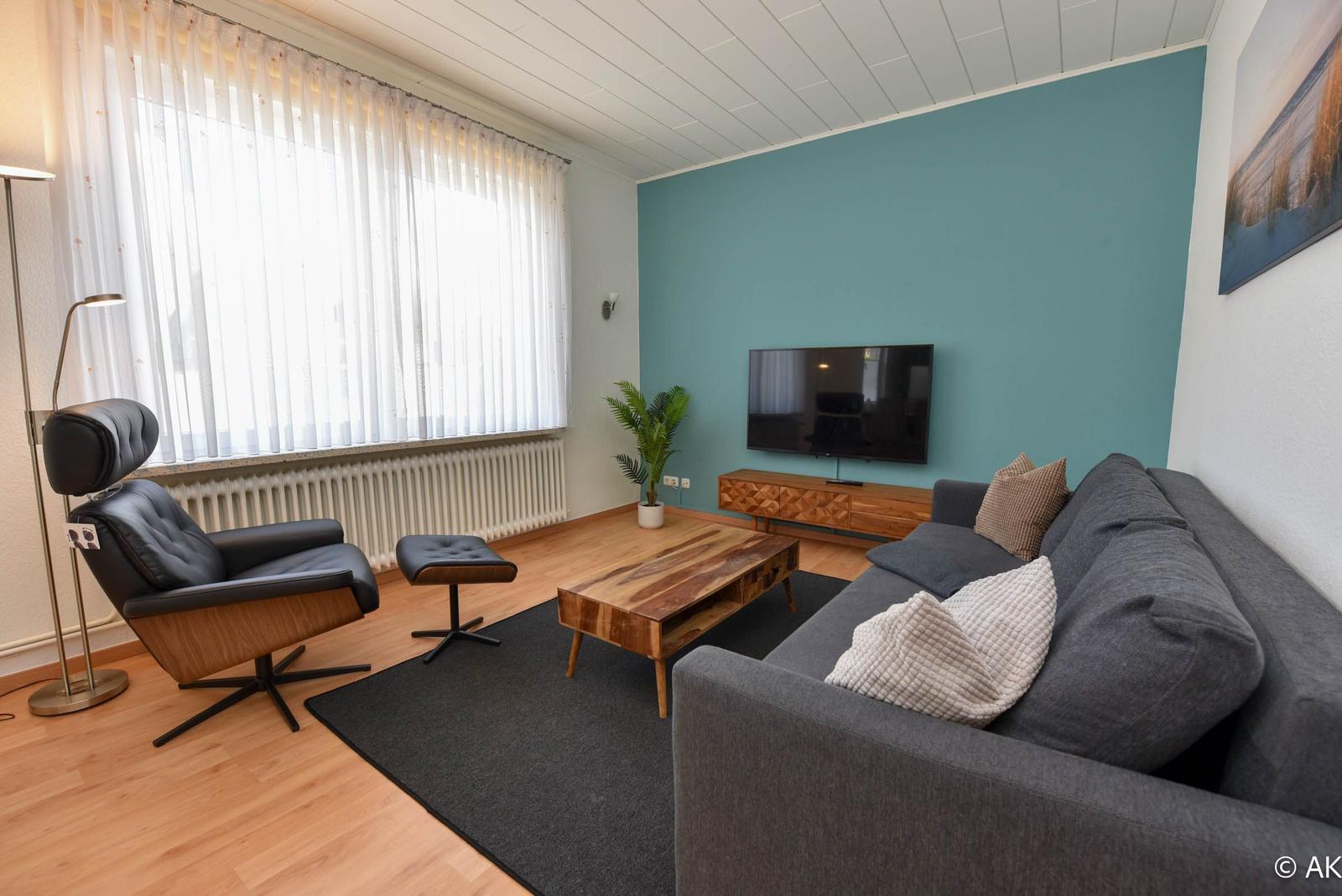 Wohnzimmer mit Sofa, Sessel, TV und Holztisch.