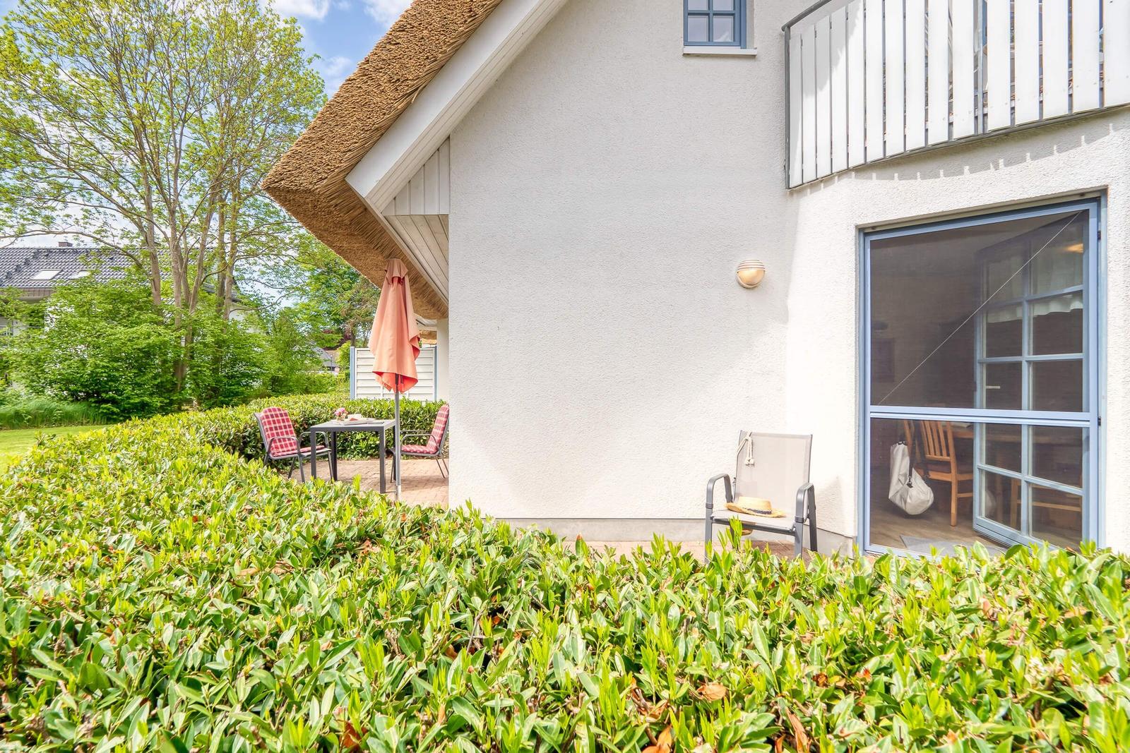 Terrasse mit Tisch, Stühlen und Sonnenschirm neben einem Haus mit Schiebetür.