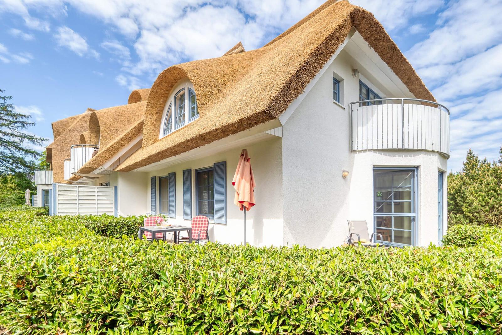Haus mit Strohdach, Balkon und Gartenmöbeln im Freien.