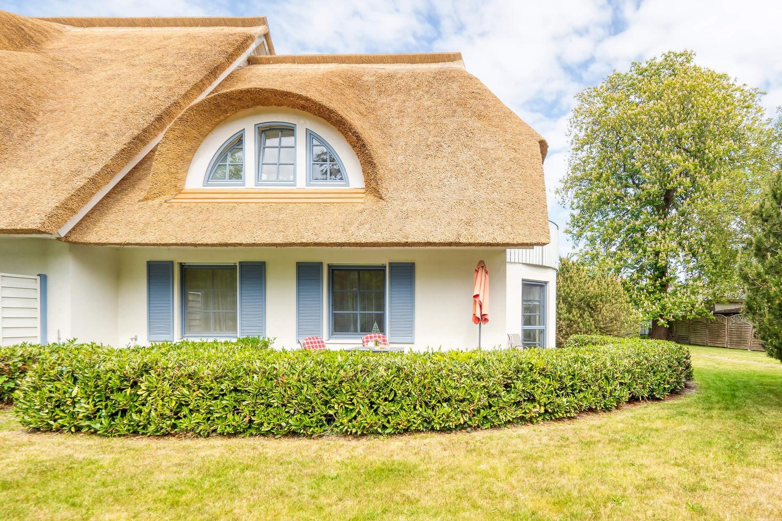 Haus mit Strohdach, blauen Fensterläden und grüner Hecke.