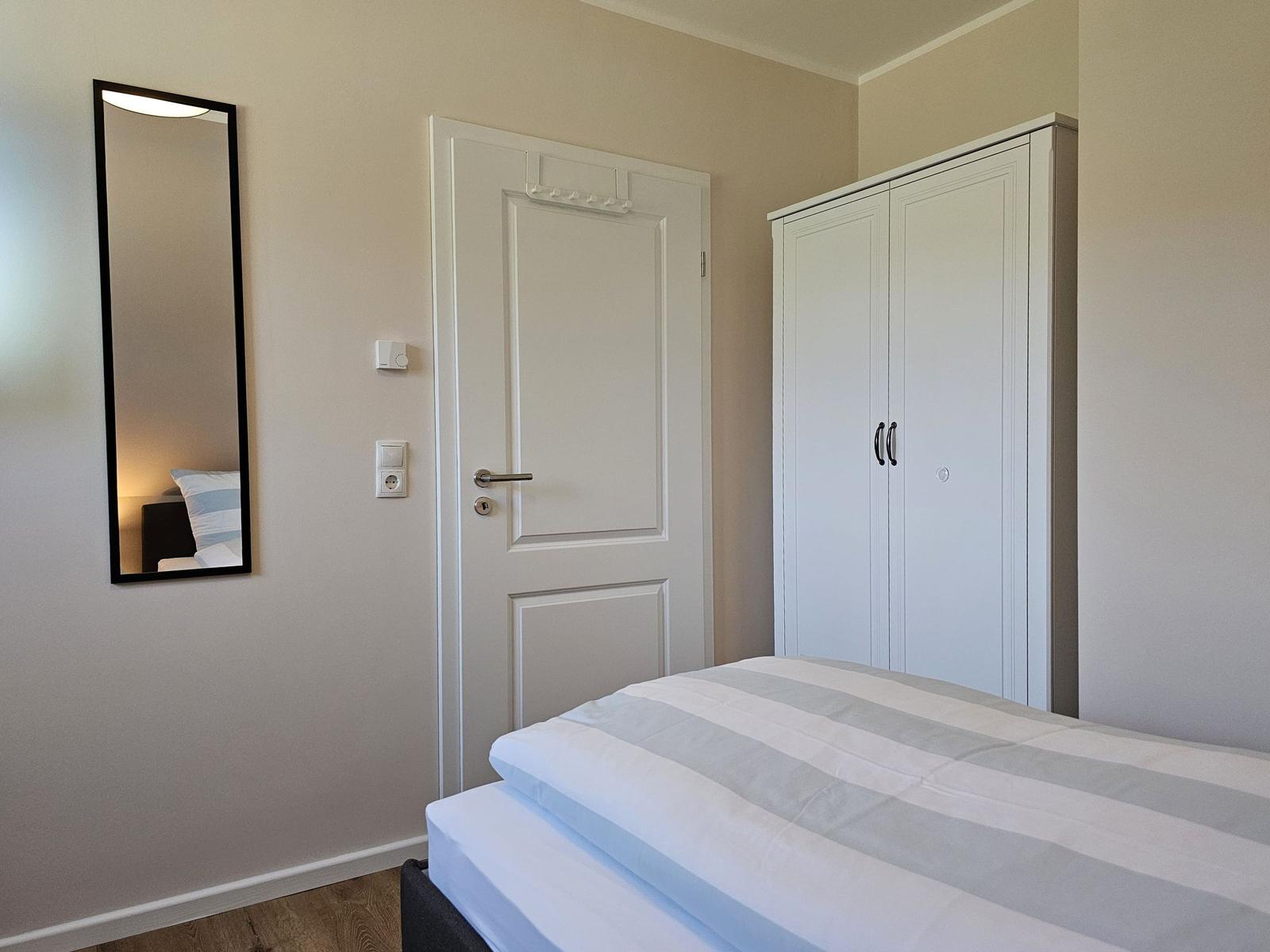 Schlafzimmer mit Bett, Kleiderschrank und Spiegel an der Wand.