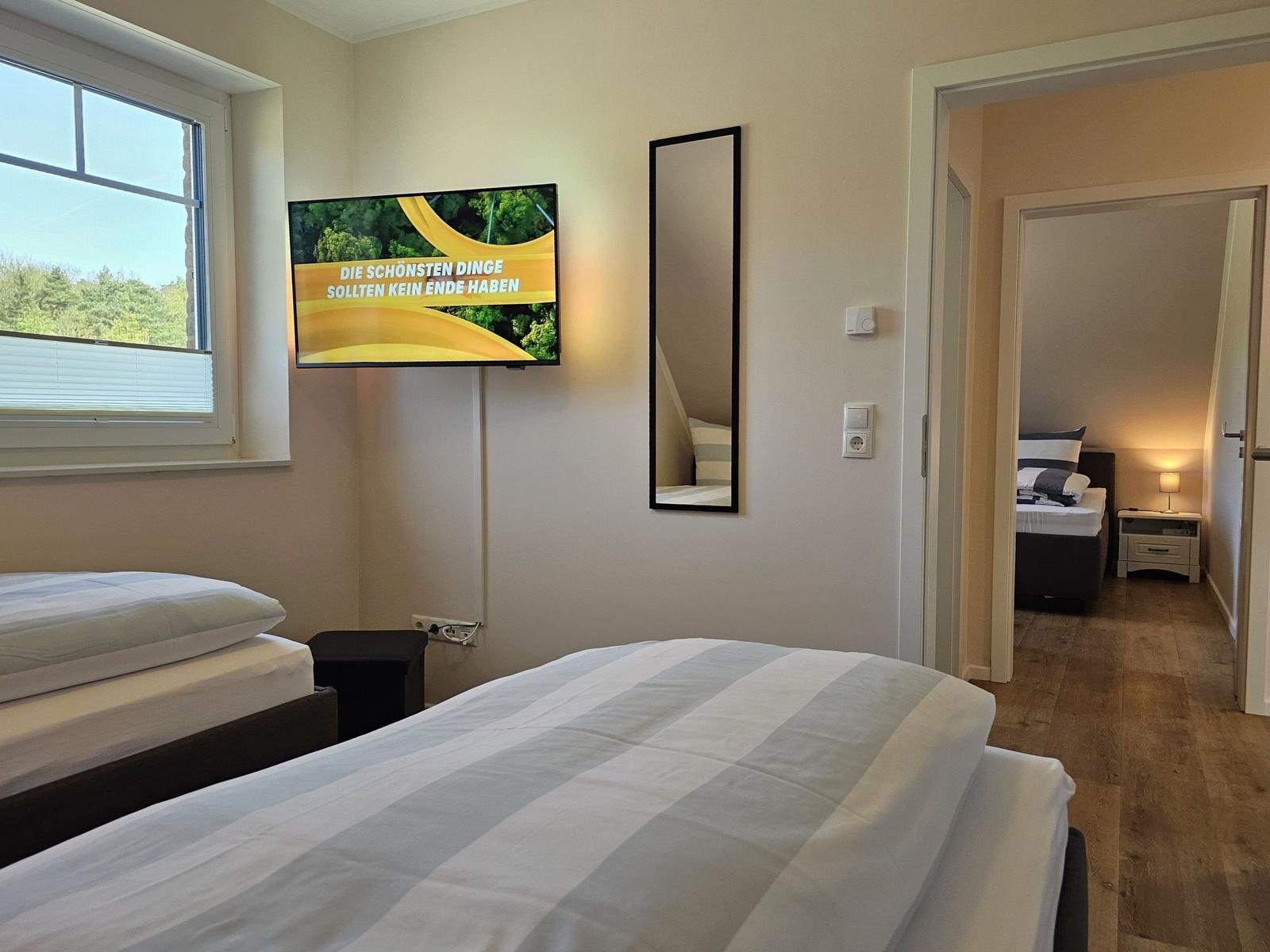 Zwei Betten, Fernseher und Spiegel. Durchgang zu weiterem Schlafzimmer.