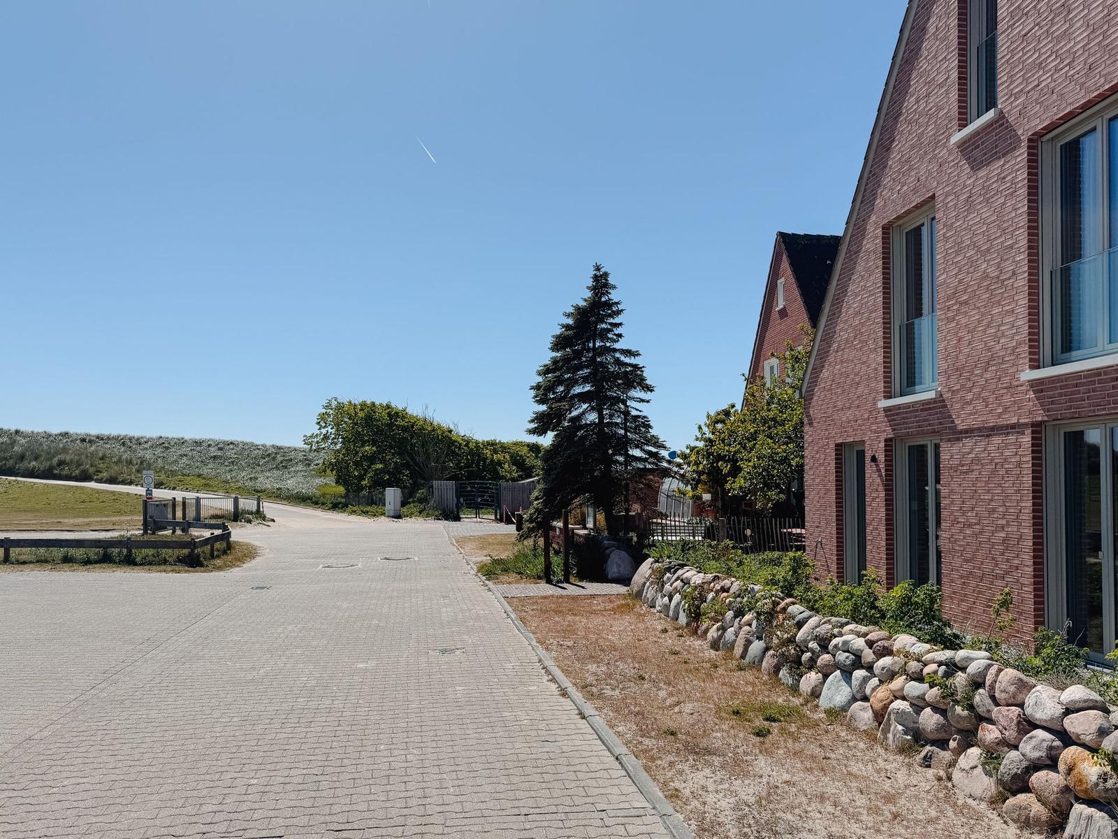 Pflasterweg neben rotem Backsteinhaus mit Steinmauer und Bäumen