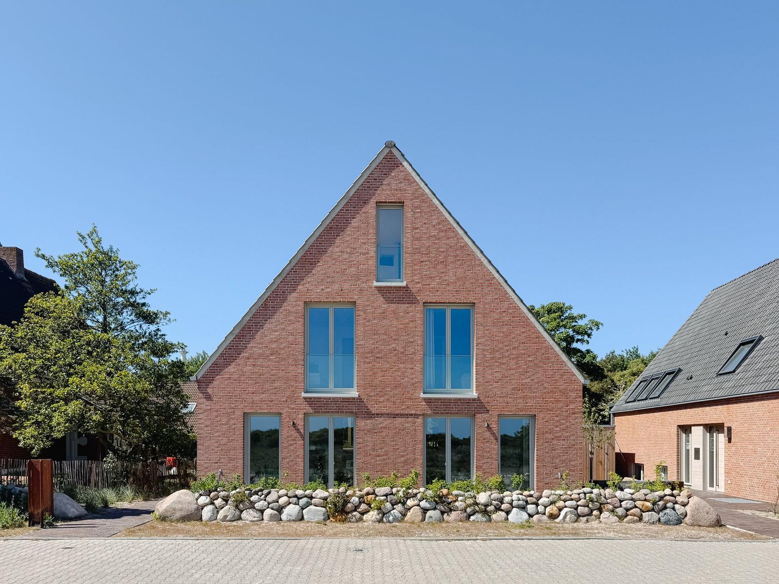 Moderne rote Backsteinhaus mit großen Fenstern und Steinmauer im Vordergrund.