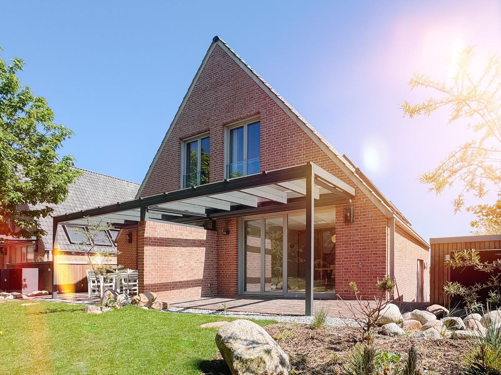 Moderne Villa mit Terrasse und Garten unter blauem Himmel.