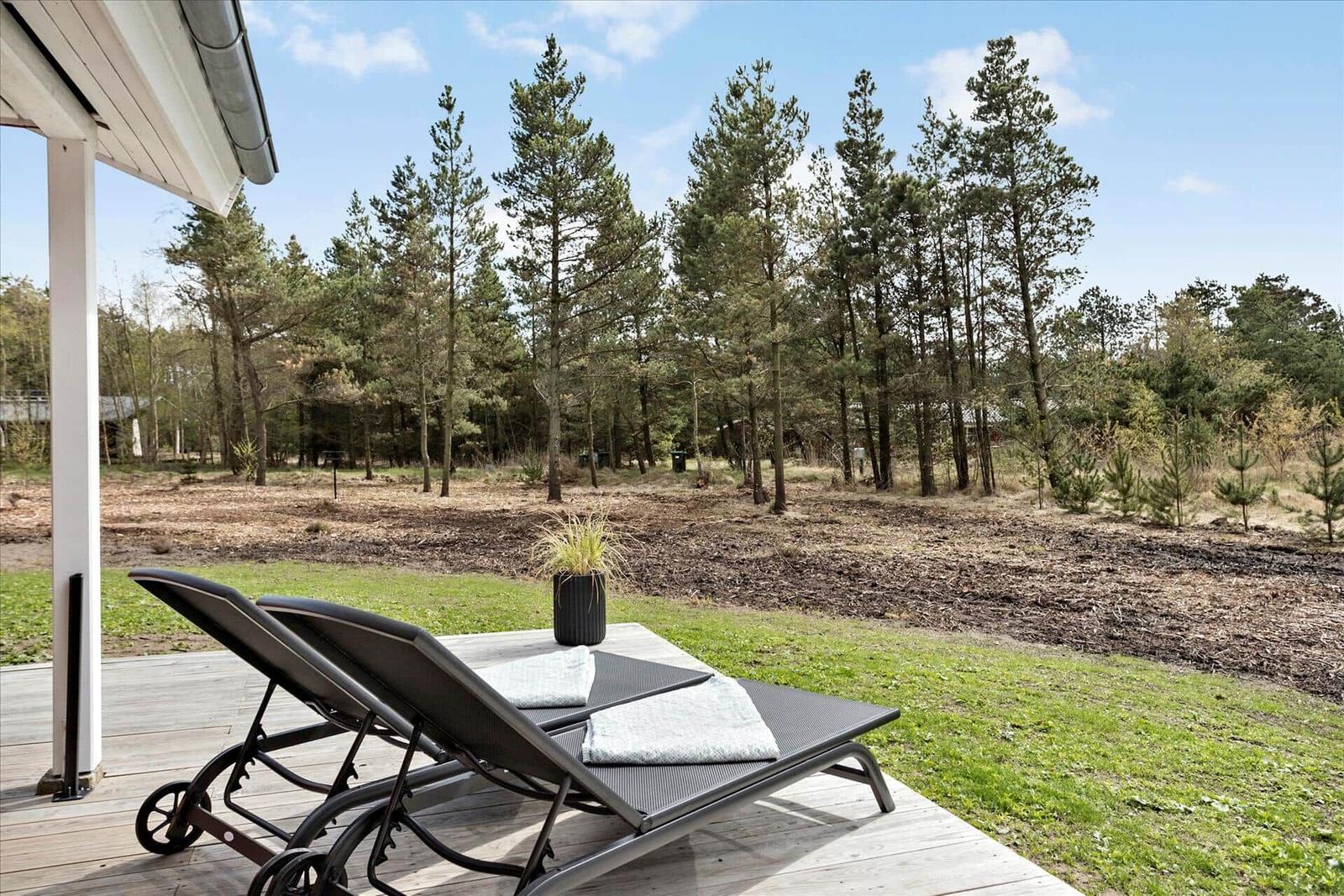 Zwei Liegestühle auf einer Terrasse mit Blick auf einen Wald.