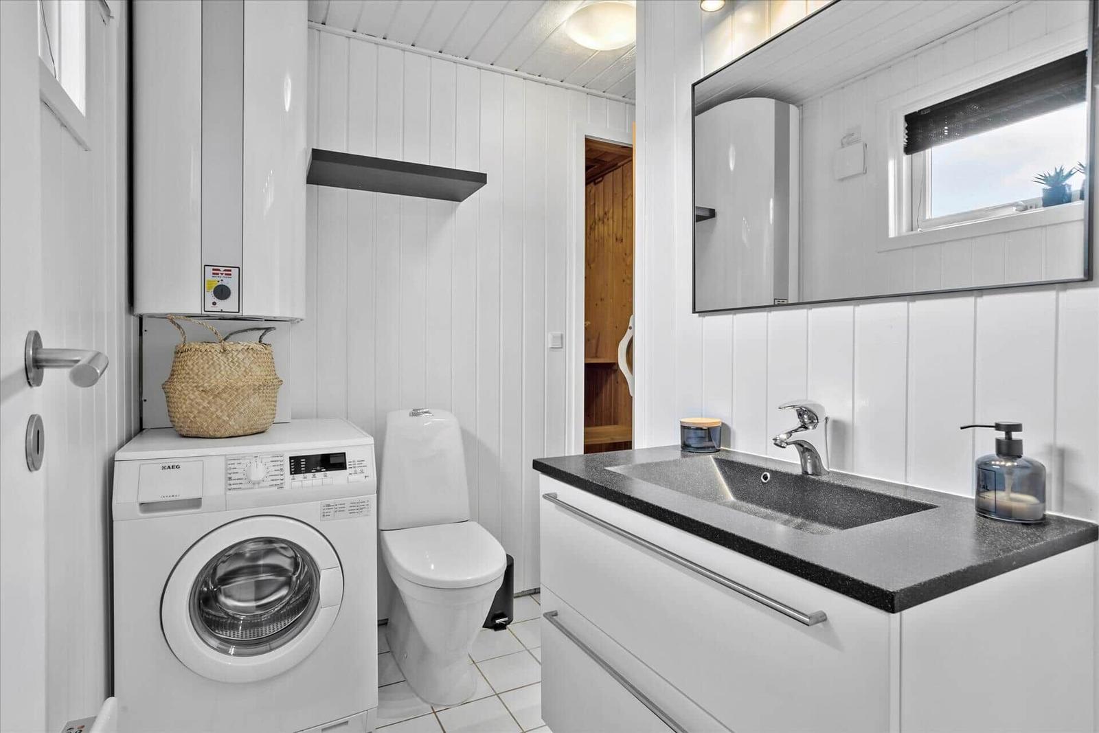 Badezimmer mit Waschmaschine, Toilette und Waschbecken mit Spiegel.
