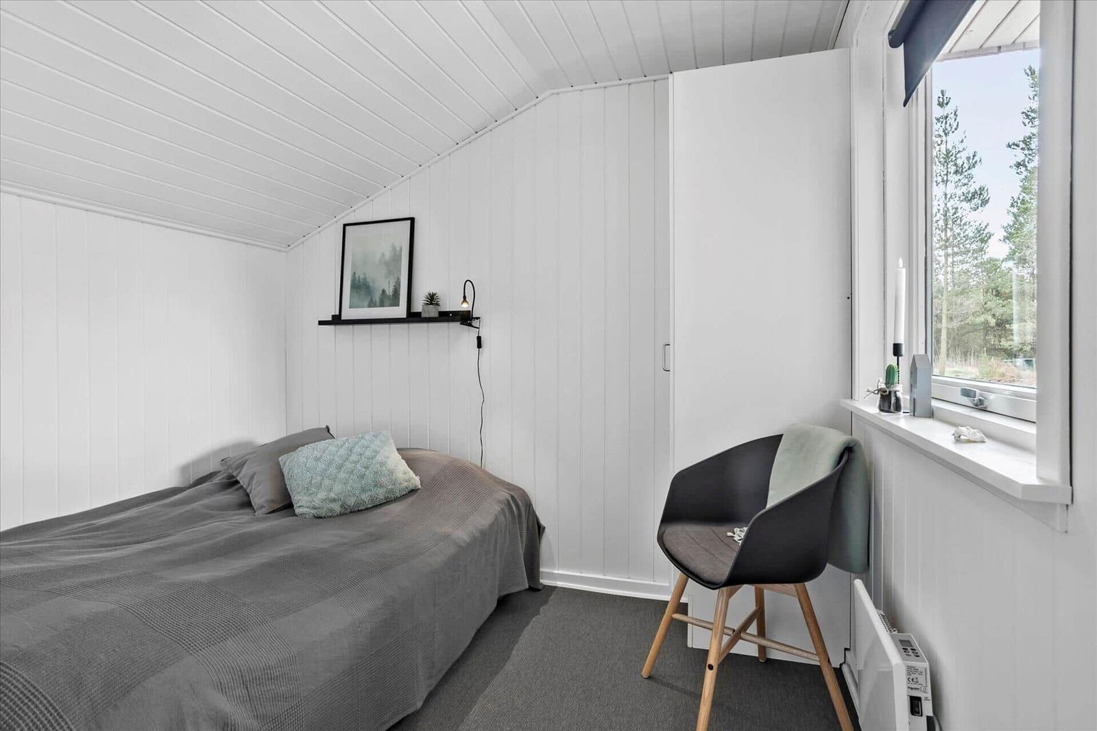Ein Schlafzimmer mit Bett, Stuhl und Fenster mit Blick auf Wald.