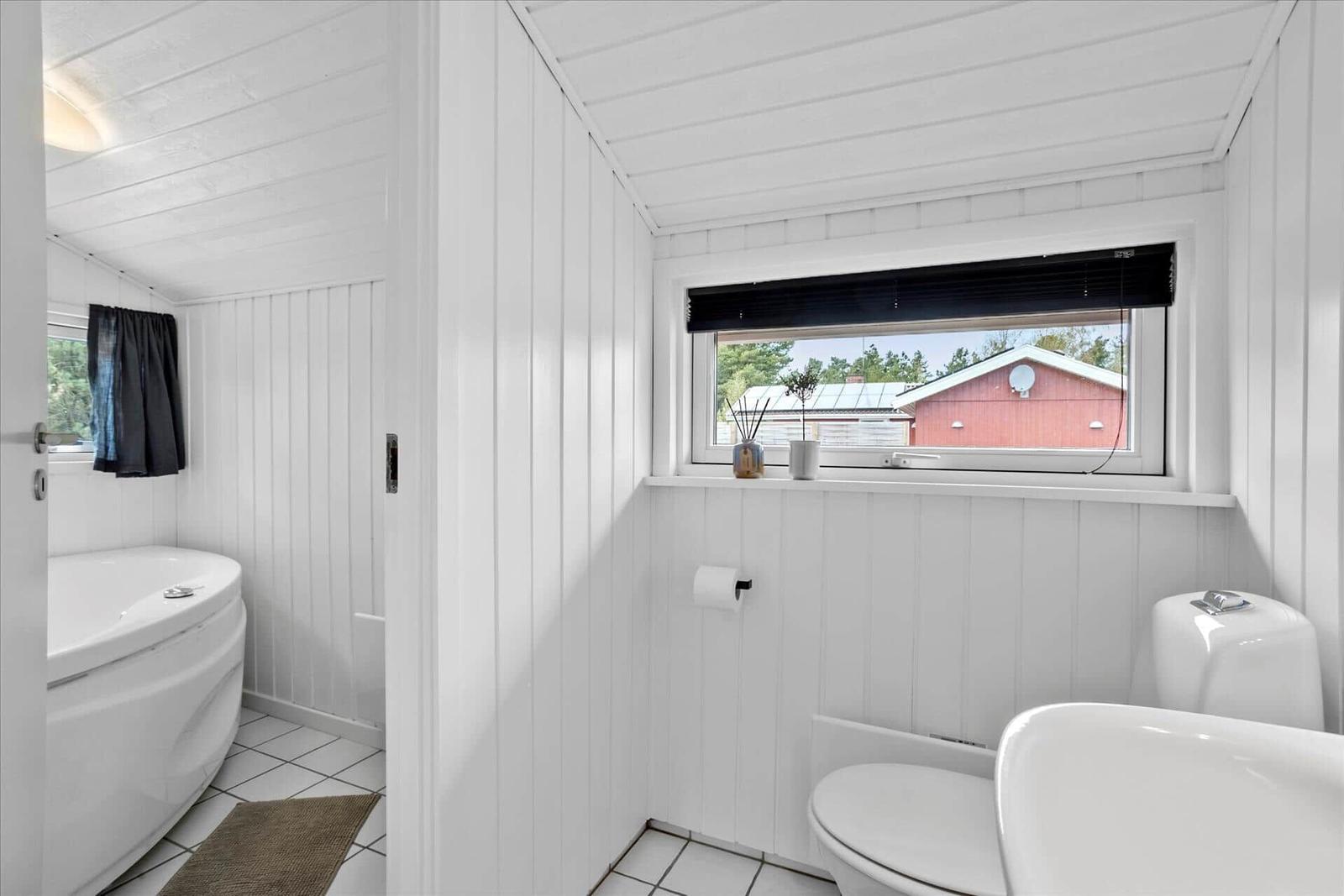 Badezimmer mit Toilette, Waschbecken und Badewanne. Fenster zeigt rotes Haus.