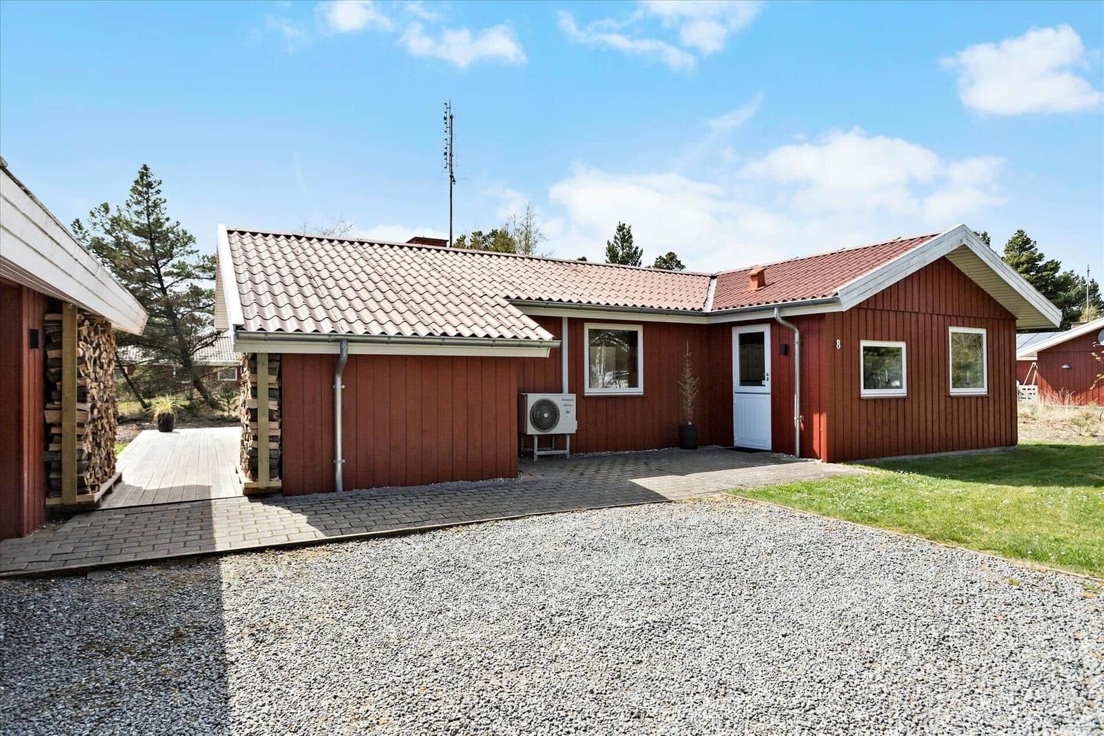 Rotes Holzhaus mit Steinmauer und Kamin, umgeben von Gras und Bäumen.