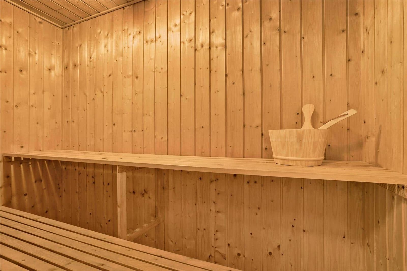 Sauna mit Holzwand, Bank und Eimer mit Löffel.