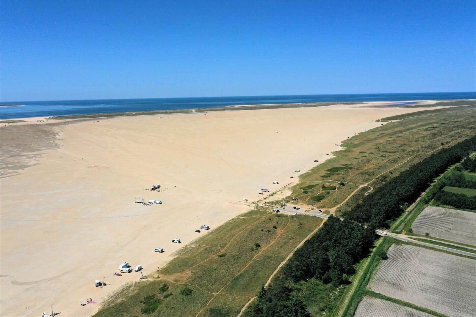Weitläufiger Strand mit Campingplätzen und grünen Hängen.