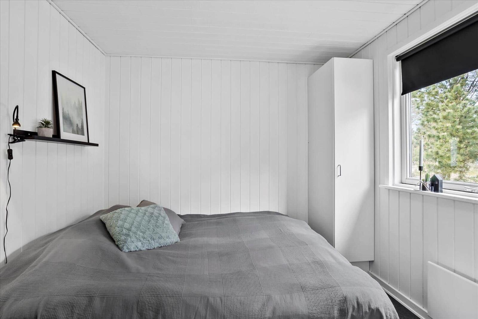 Schlafzimmer mit Bett, Schrank und Fenster mit Blick auf Bäume.