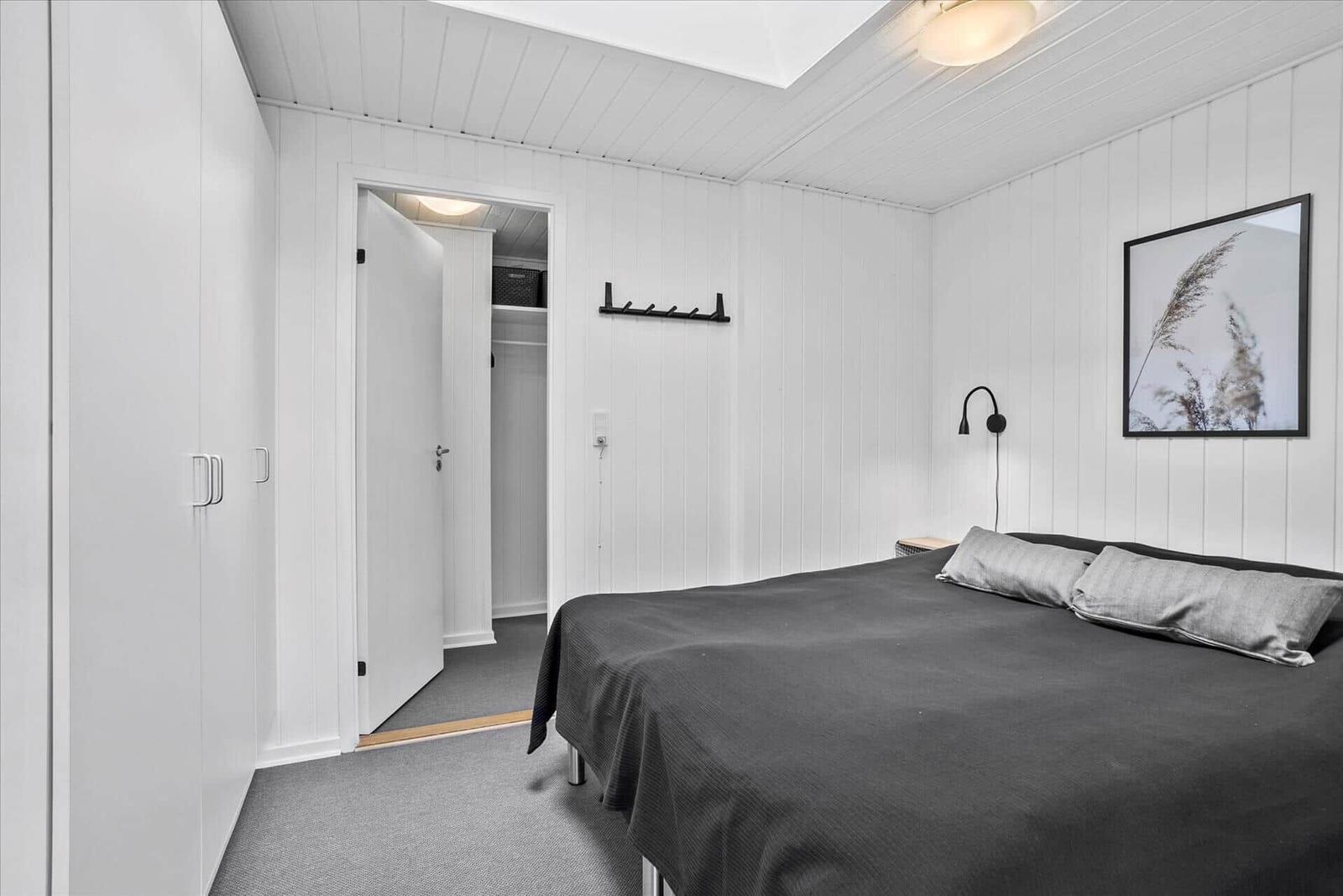Schlafzimmer mit Bett, Kleiderständer und Wandbild.