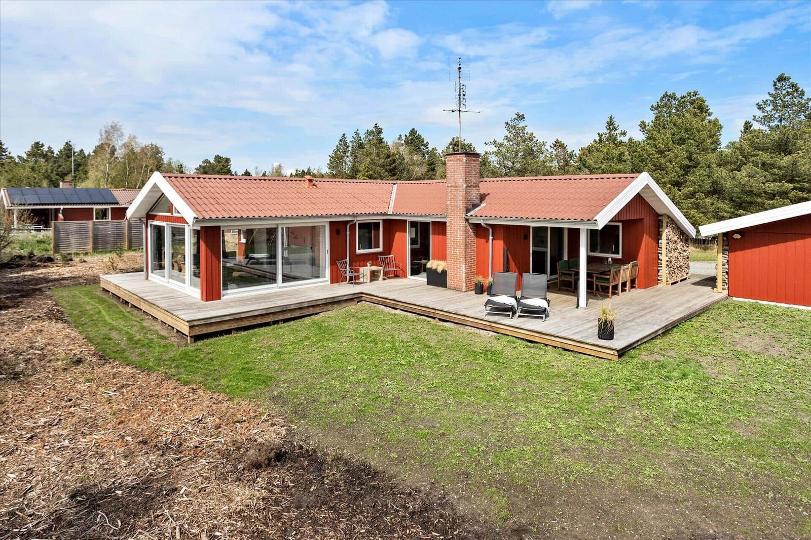 Rotes Ferienhaus mit Holzterrasse, Garten und Grillplatz. Umgeben von Wald.