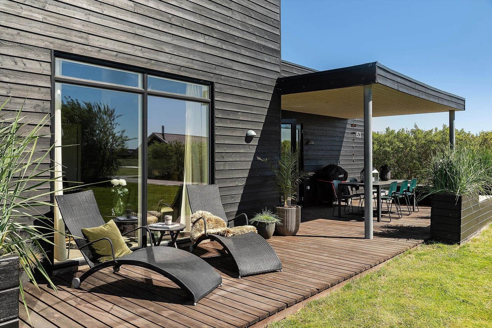 Terrasse mit Liegestühlen und Grillplatz. Holzdeck und Pflanzen umgeben die Außenecke.
