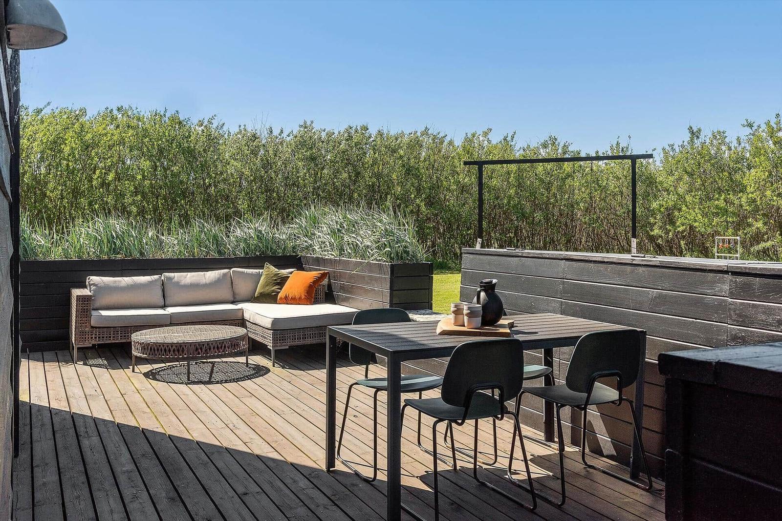 Terrasse mit Sitzgruppe, Tisch und Stühlen. Hintergrund: grüne Vegetation.