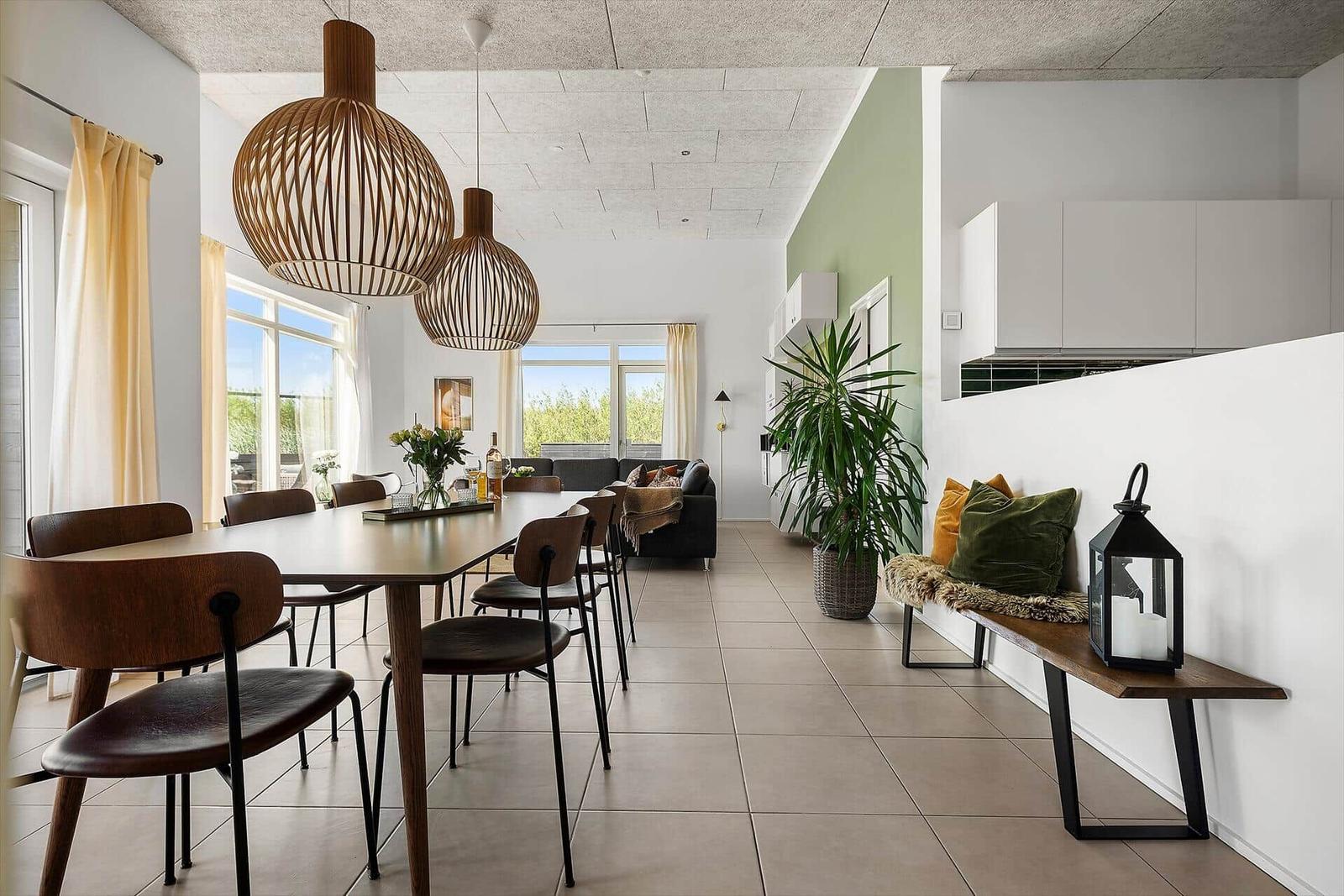 Essbereich mit Tisch, Stühlen und hängenden Lampen. Wohnbereich mit Sofa und Pflanze.