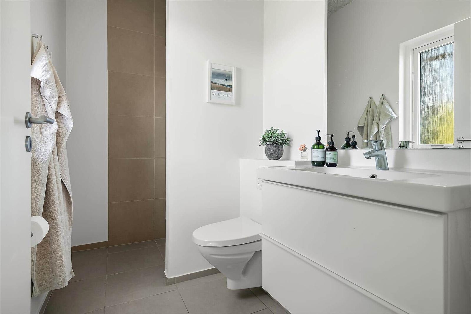 Badezimmer mit Waschbecken, Toilette und Dusche. Fenster mit getöntem Glas.