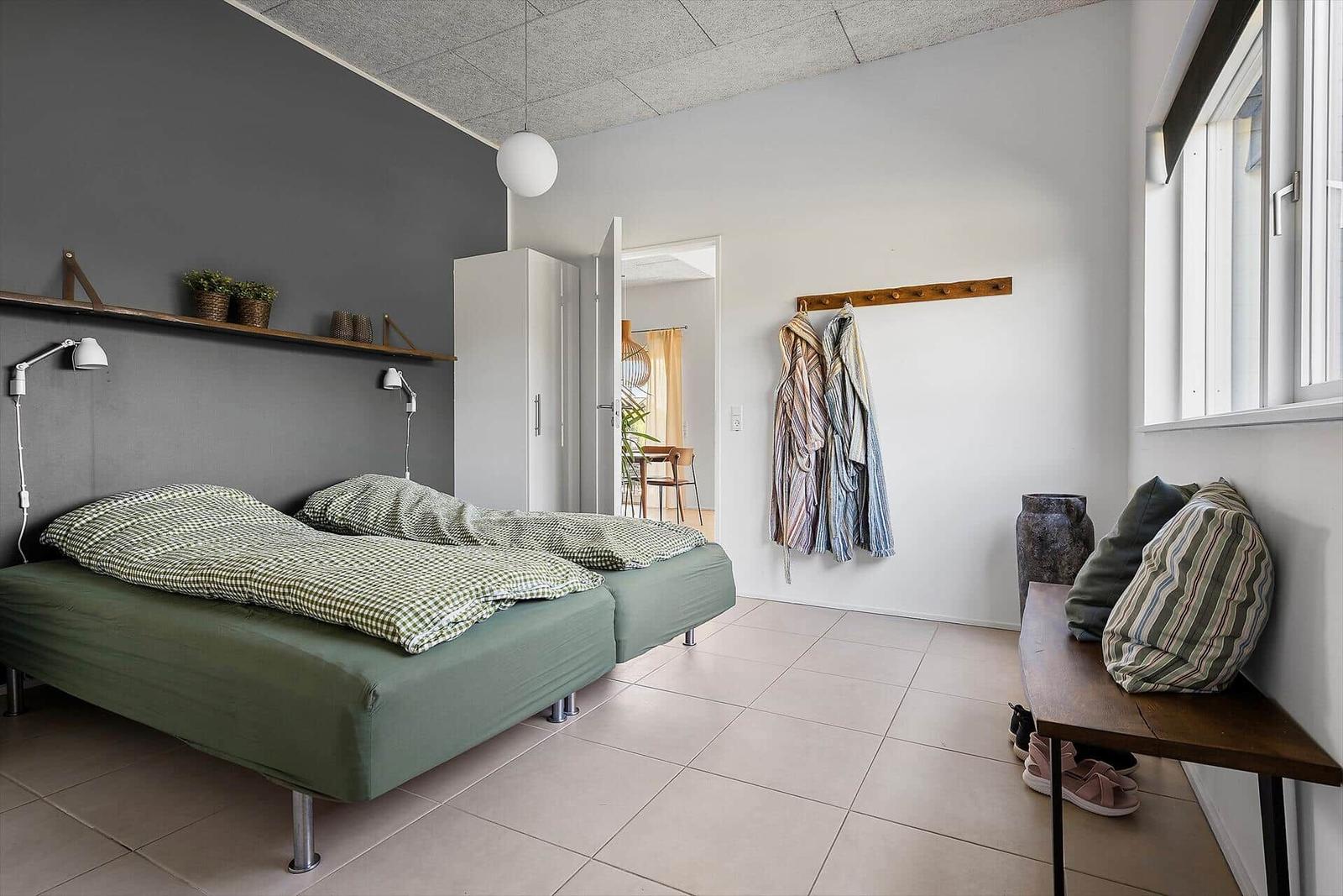 Zimmer mit Bett, Kleiderhaken und Fenster. Blick in angrenzenden Raum.