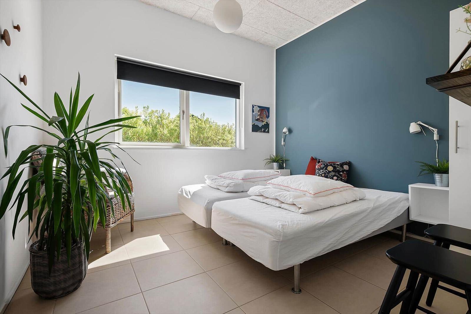 Zwei Einzelbetten mit weißer Bettwäsche, blaue Wand, Fenster mit Blick auf Grün.
