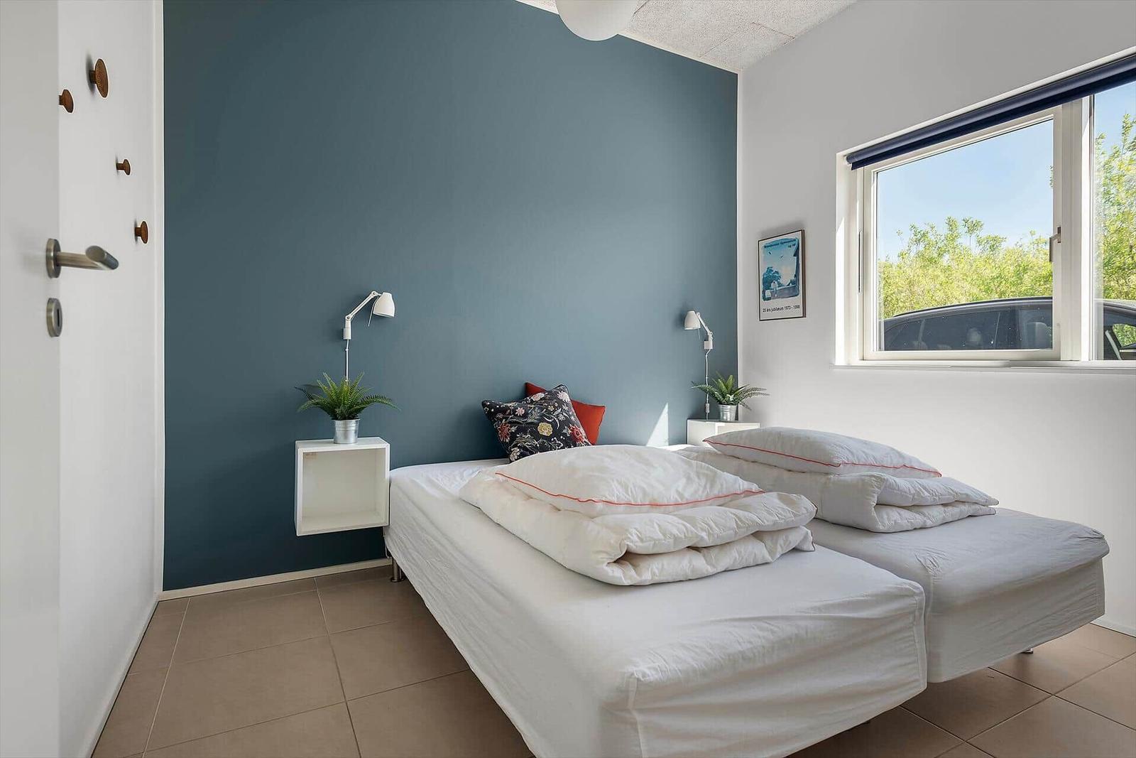 Zimmer mit zwei Betten, blauer Wand und Fenster mit Blick auf Grün.