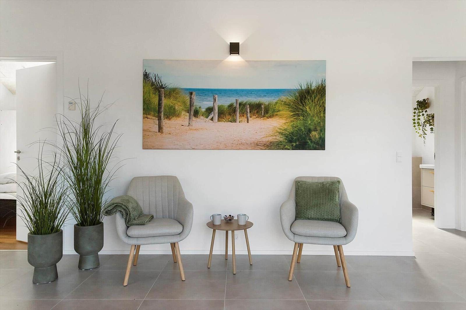 Two gray chairs sit before a wall with a beach picture. Between them a small table.