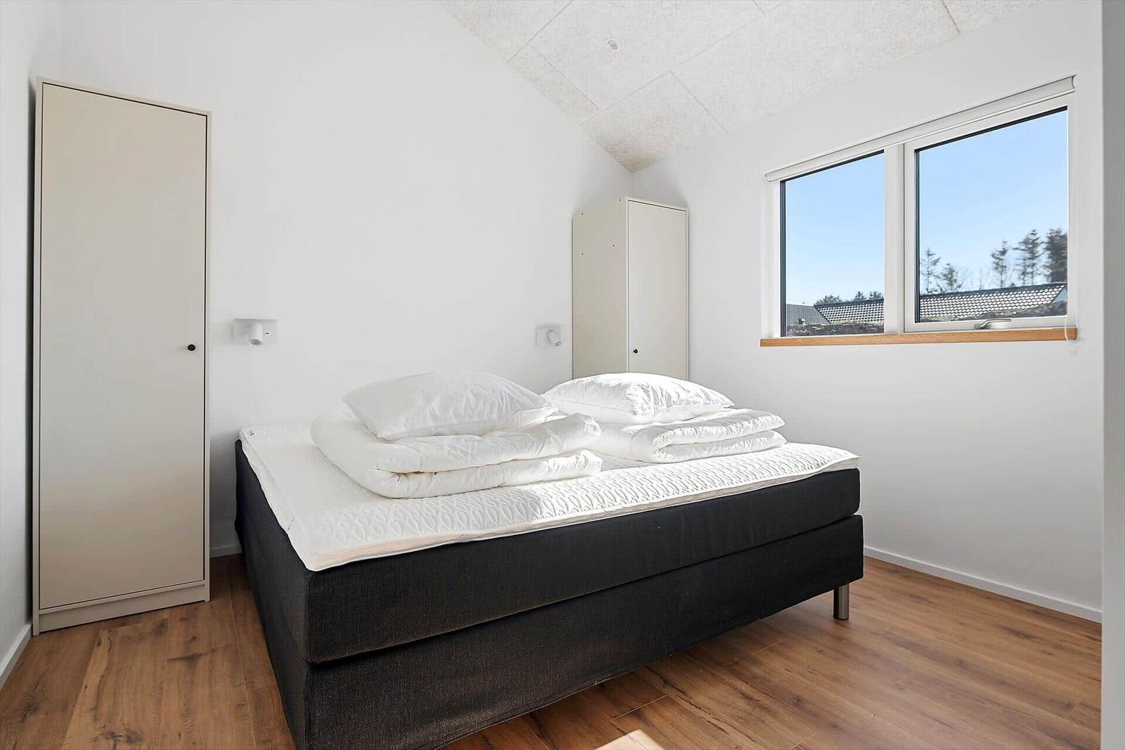 Bedroom with bed, two closets, and window overlooking rooftops.