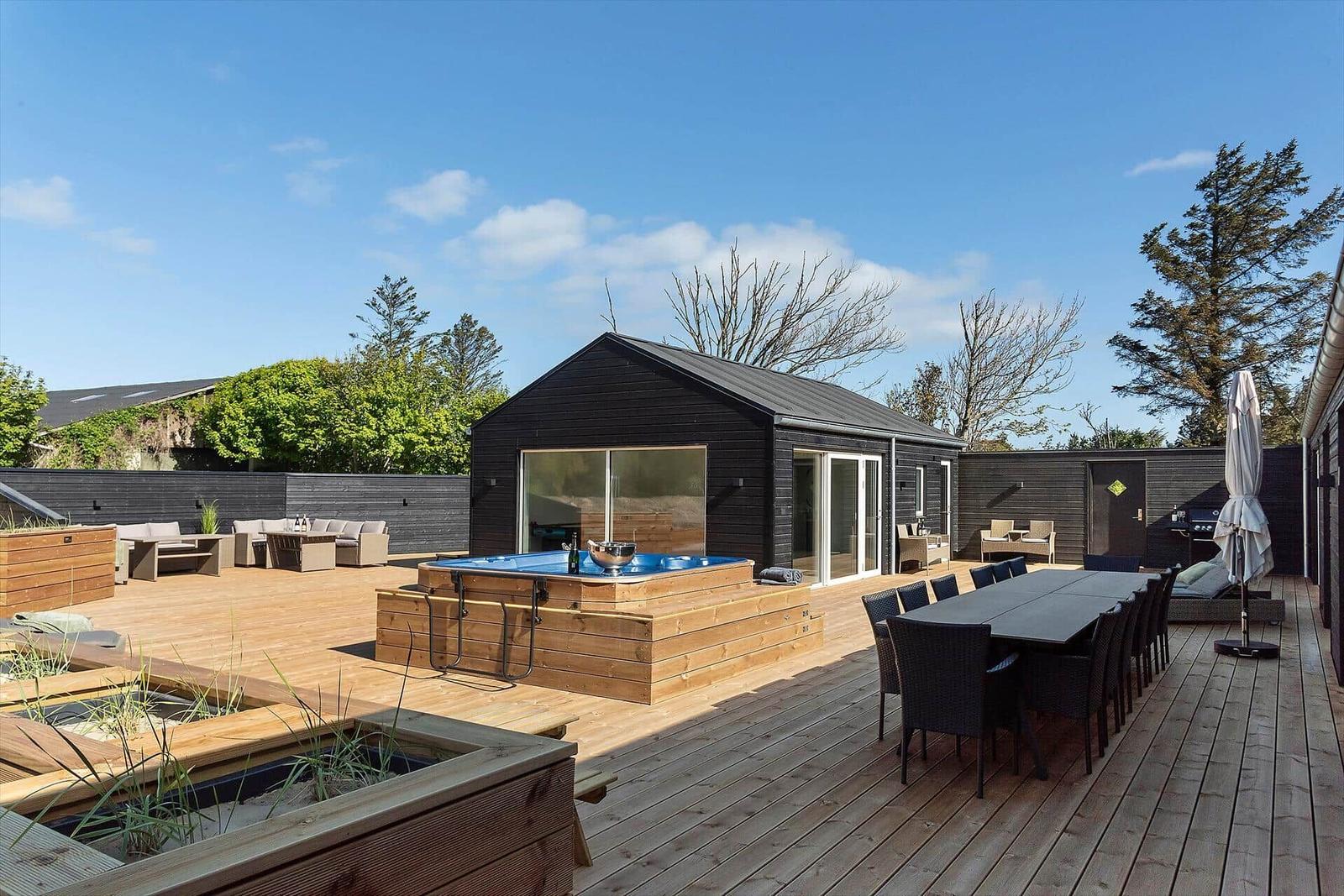 Deck with hot tub, dining table, and seating. Black house with glass doors.