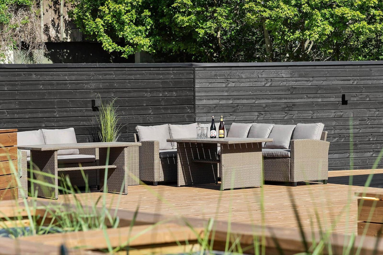 Terrace with garden furniture, table, and drinks in front of dark wooden fence.