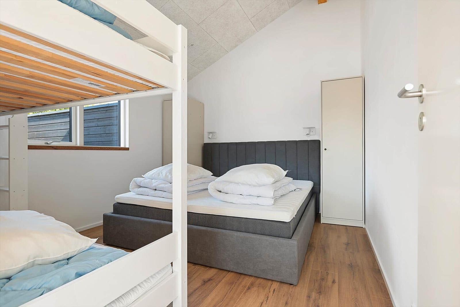 Bedroom with double bed and loft bed. Wooden floor and window.