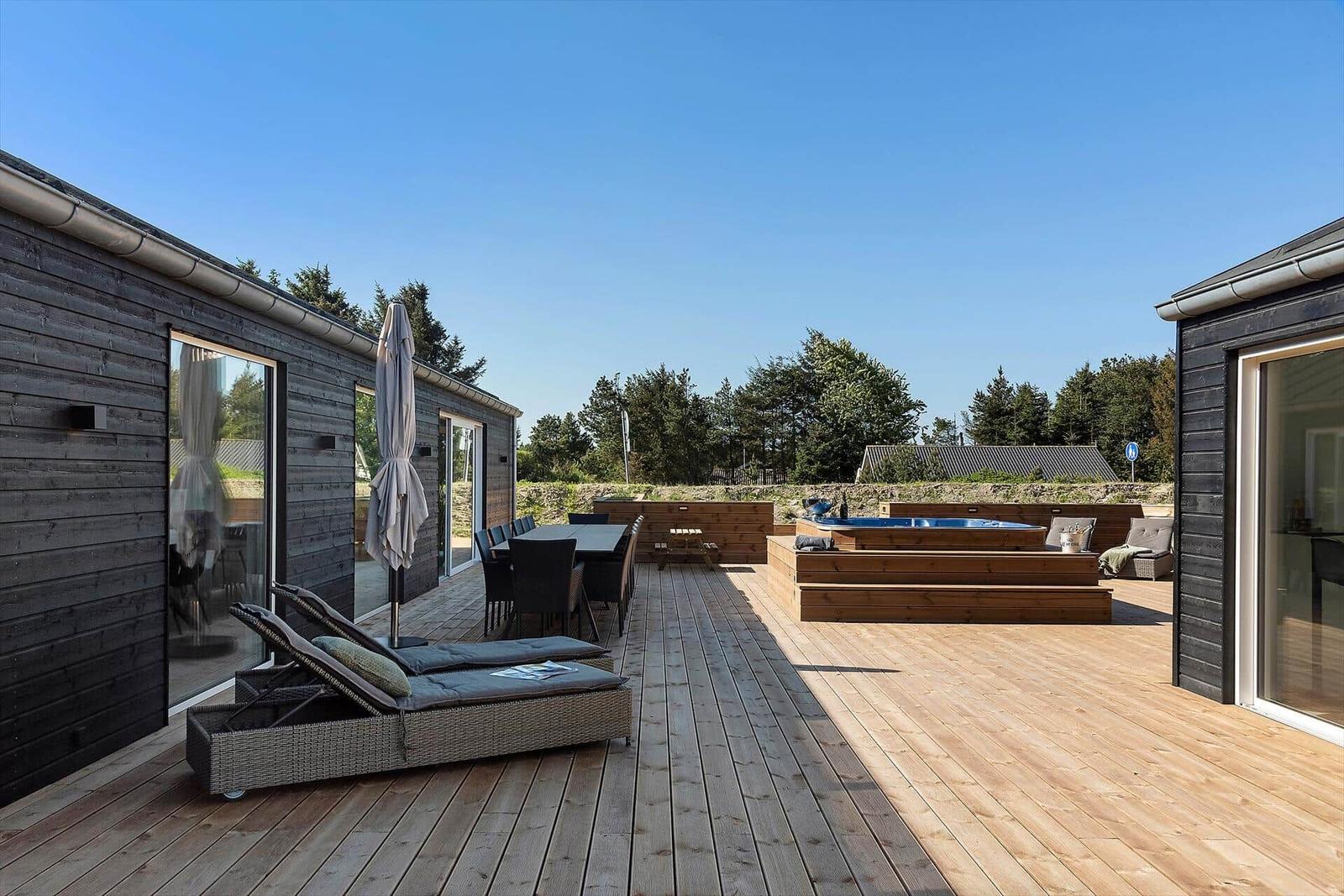 Deck with loungers, table and hot tub. Wooden deck, garden furniture, and forest in the background.