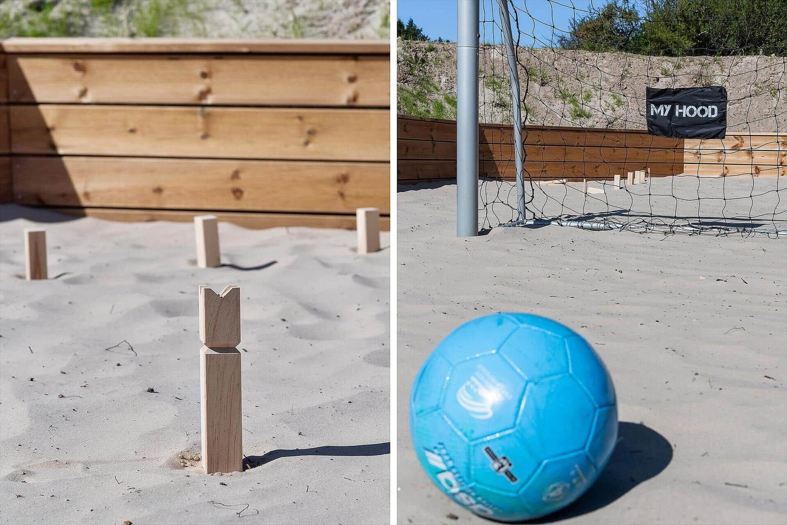 Sandy area with wooden toys and soccer goal. A blue ball lies in front of the goal.