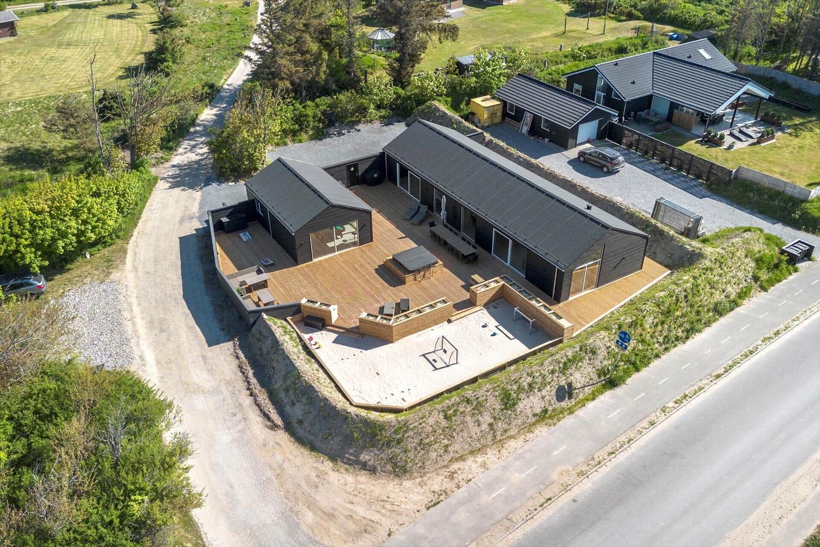 Modern house with large wooden terrace, pool area, and surrounding green areas.