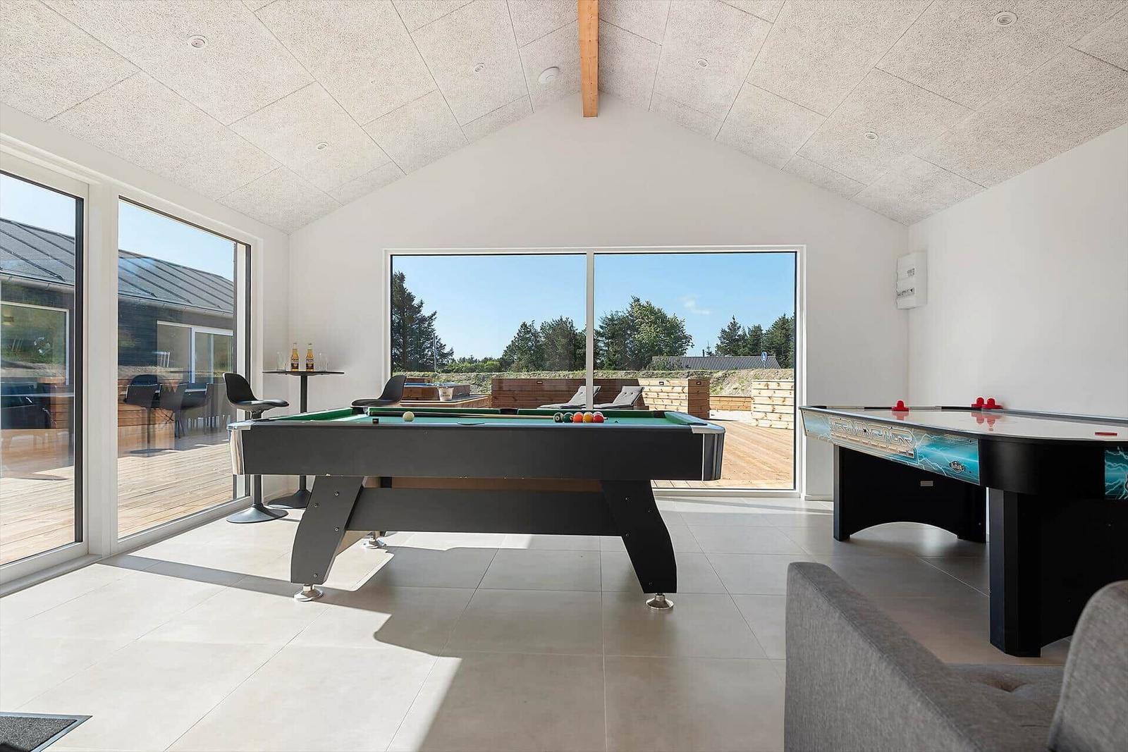 Room with pool table and air hockey table, large windows, view of terrace.