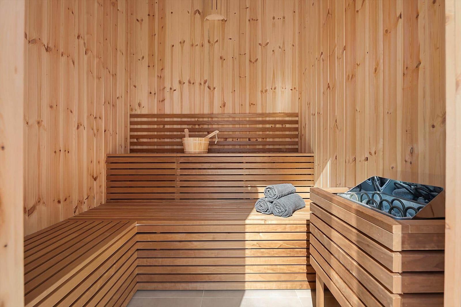 Wood sauna with multiple seating levels, towels, and water bucket.