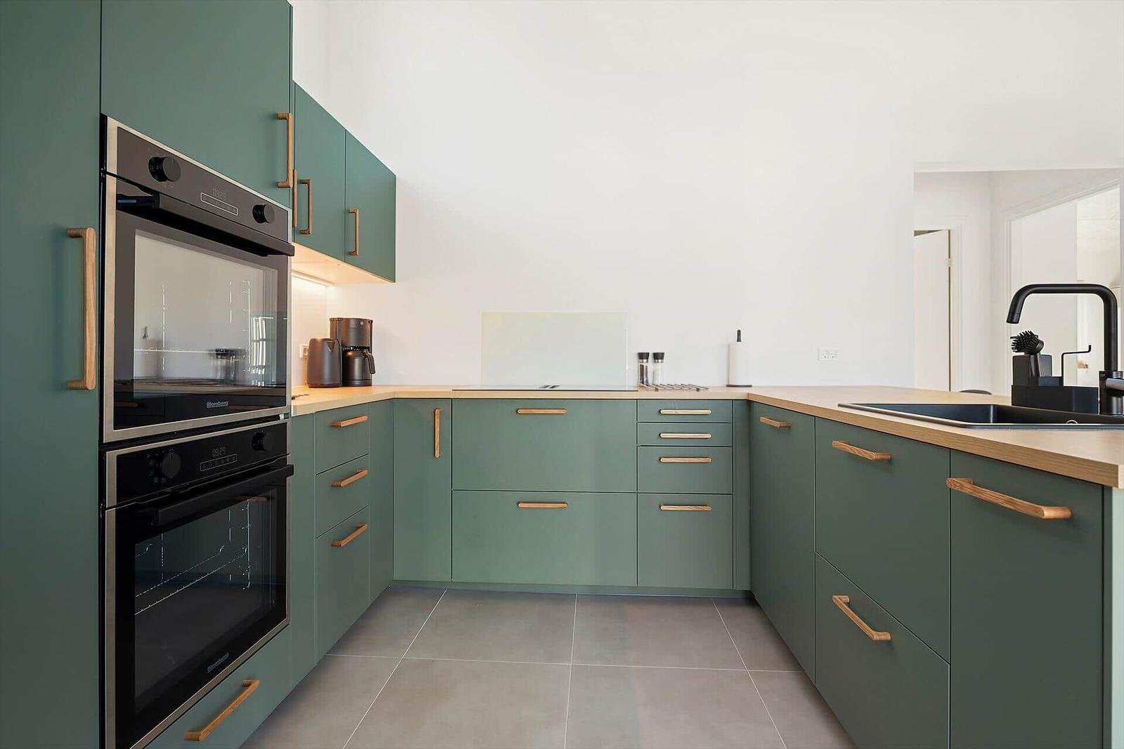Kitchen with green cabinets, wooden handles, and built-in oven.