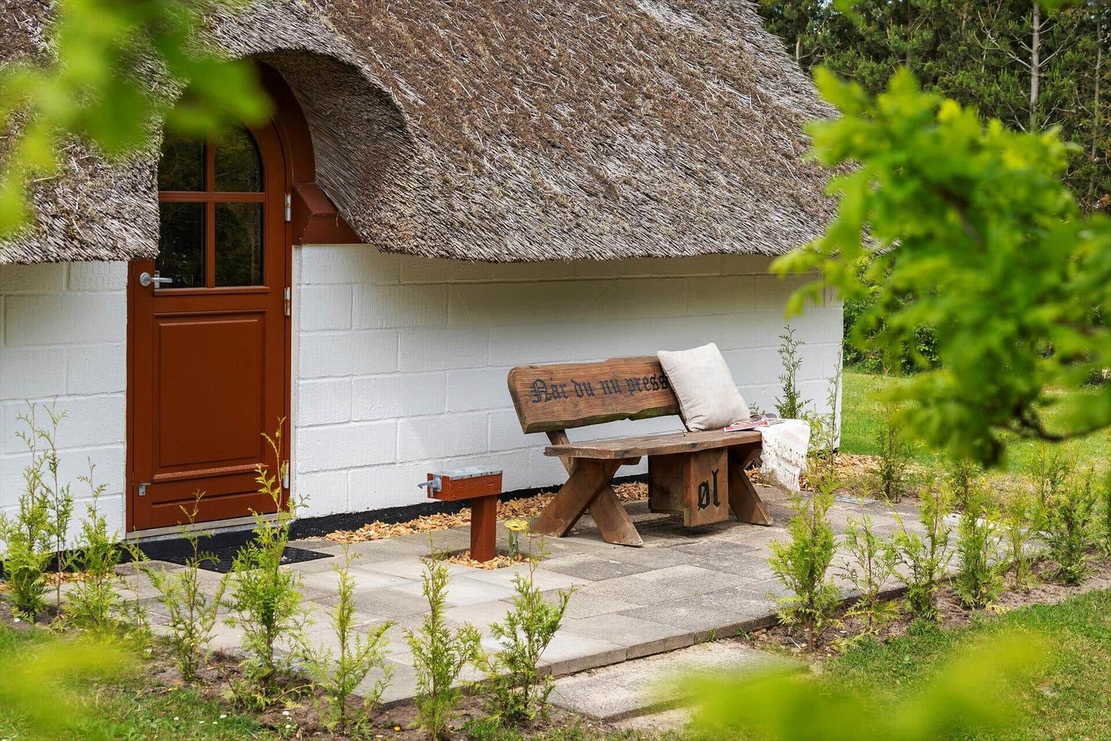 Hütte mit Strohdach, brauner Tür und Holzbank mit Kissen.