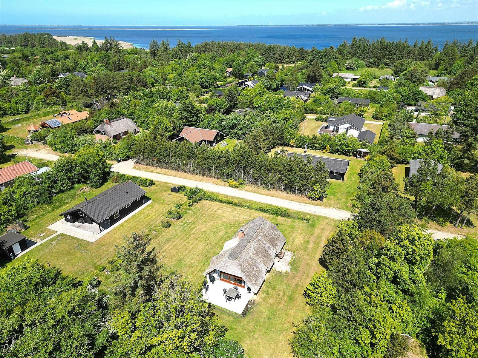 Haus mit Strohdach und Terrasse, umgeben von Grün und Wald, mit Blick auf das Meer.