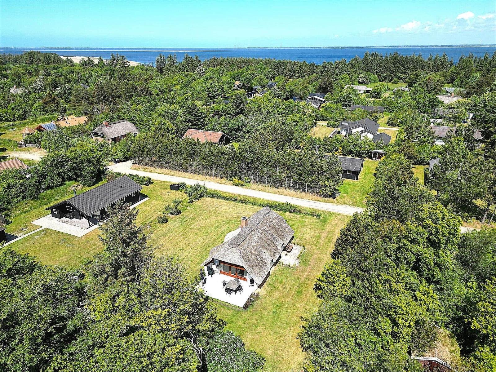 Haus mit Dachterrasse, umgeben von Grünflächen und Wald, Blick auf Meer.