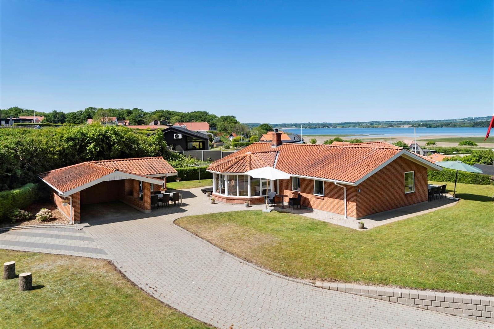 Rotes Backsteingebäude mit Terrasse und Garten. Blick auf Wasser und Grünflächen.