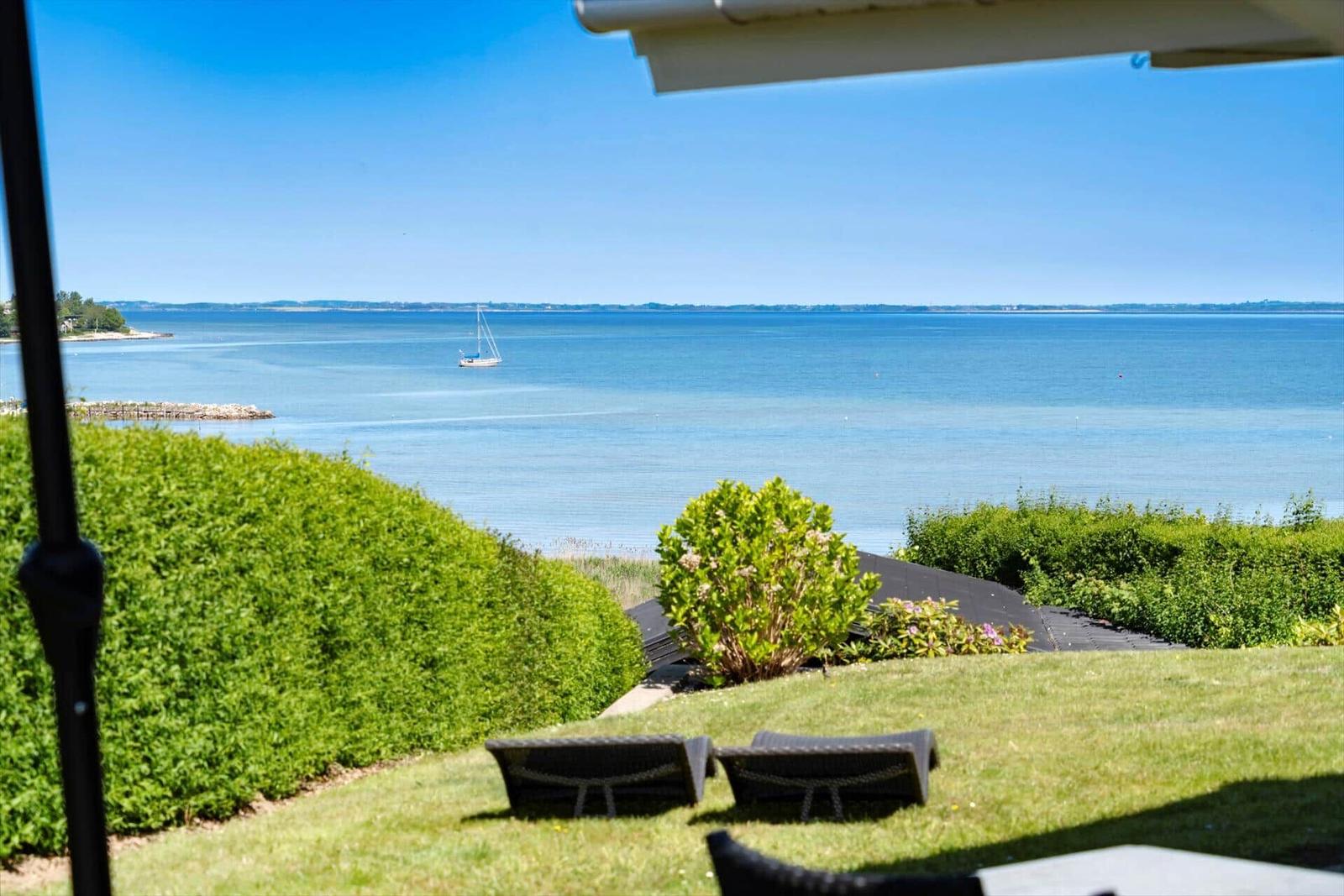 Terrasse mit Liegestühlen und Blick aufs Meer mit Segelboot.