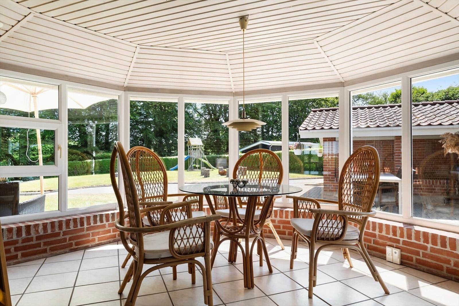Glashaus mit Sitzgruppe, Blick auf Garten und Terrasse.