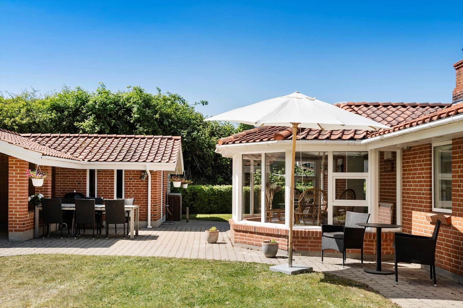 Terrasse mit Sitzgruppe, Sonnenschutz und Grillbereich. Grünflächen und Terrakottadach.