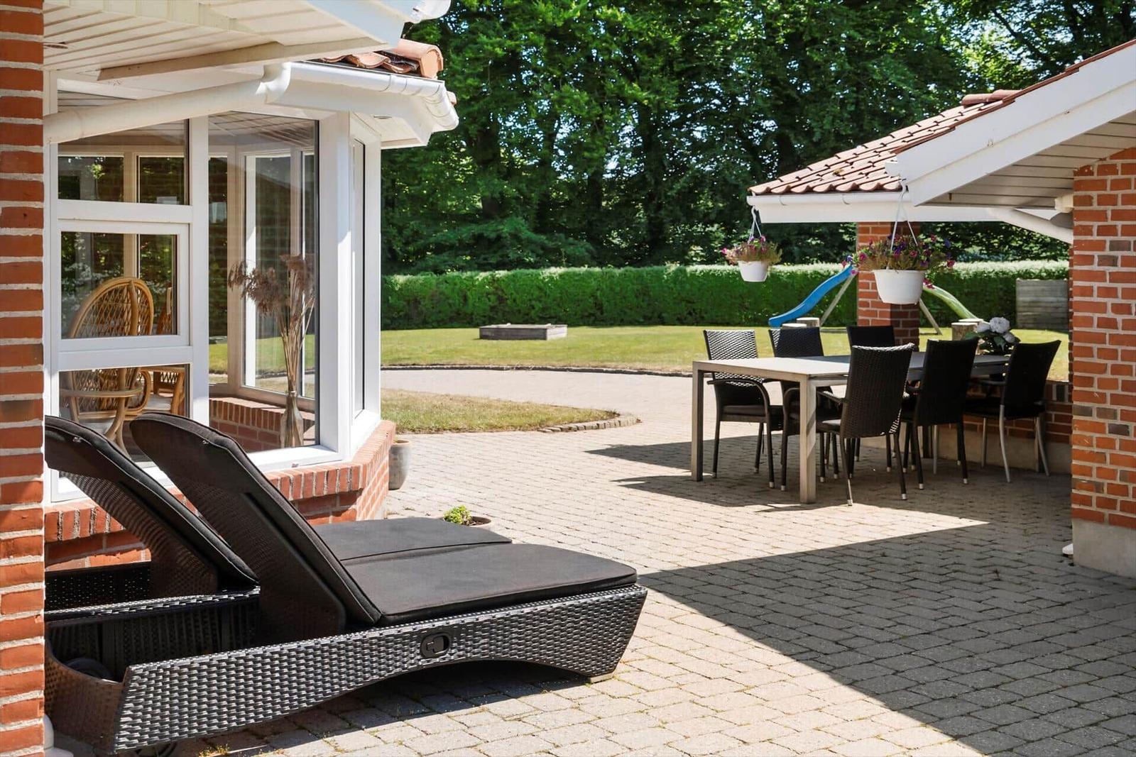 Terrasse mit Liegen, Tisch und Stühlen. Hinterhof mit Rasen und Spielplatz.