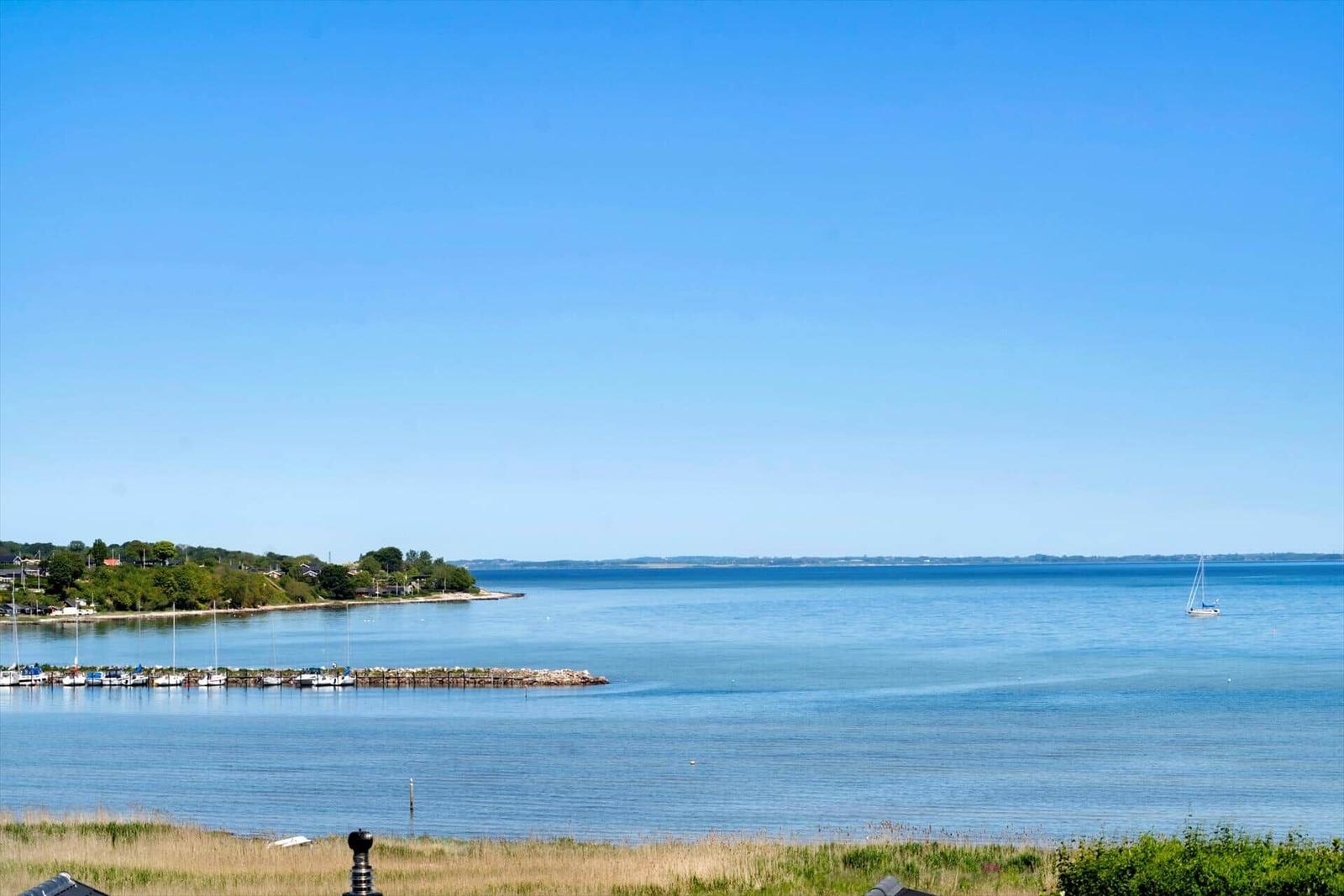 Blick auf ruhiges Wasser mit Segelboot und Bootshafen am Horizont.