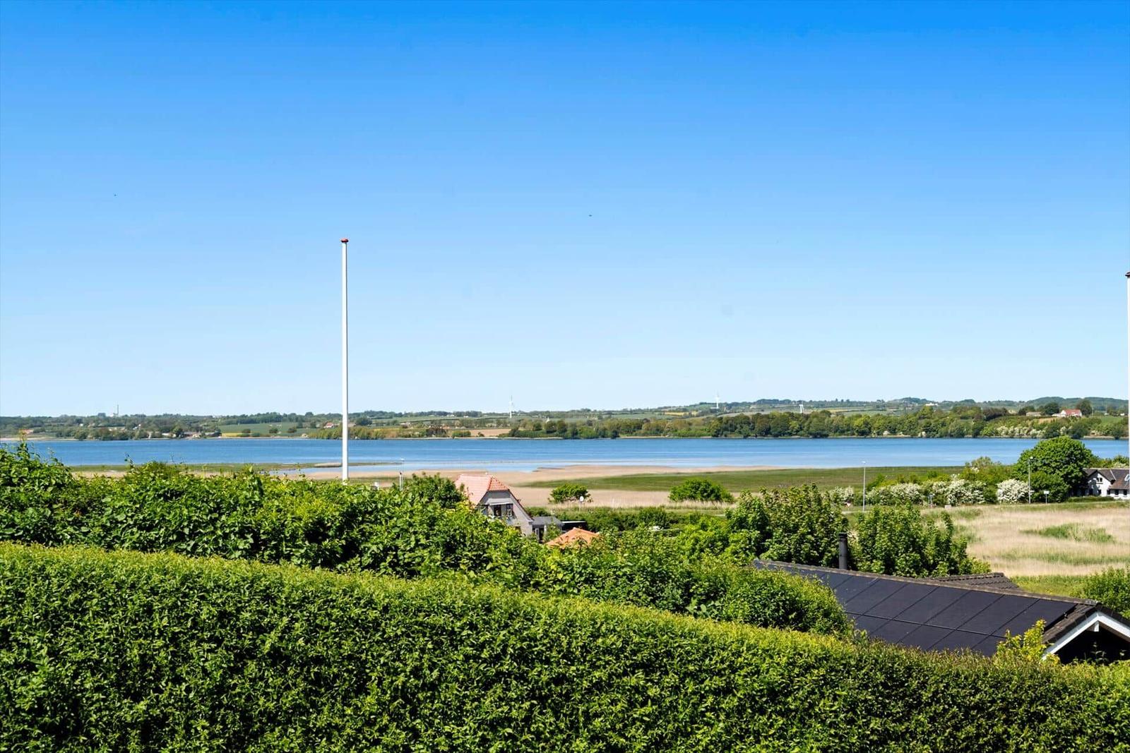 Weitläufiger Blick auf einen See mit grünen Uferzonen und einem hohen Mast im Vordergrund.